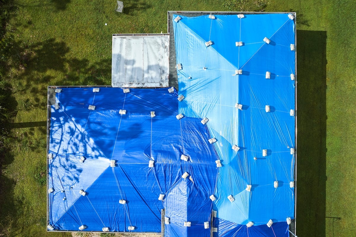 Top view of leaking house roof covered with protective tarp sheets