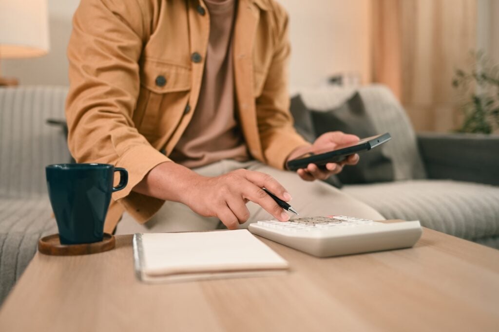 A Close-up of a man in a casual outfit calculates expenses using a calculator, Taking control of personal finances at home.