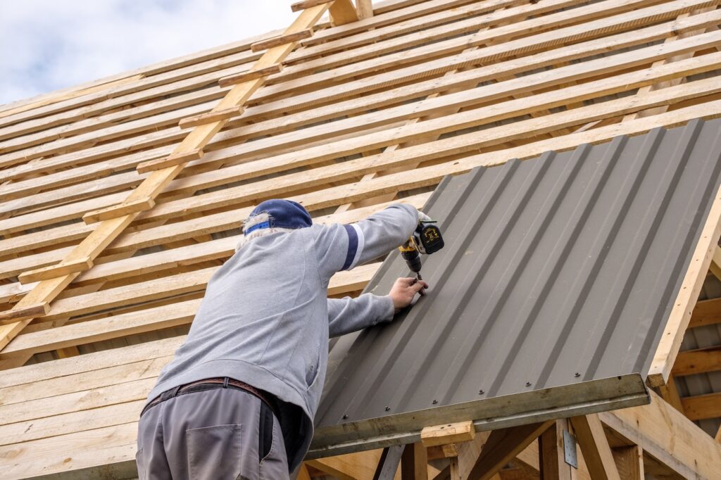builder man with a screwdriver screwing a roofing sheet to the roof.
