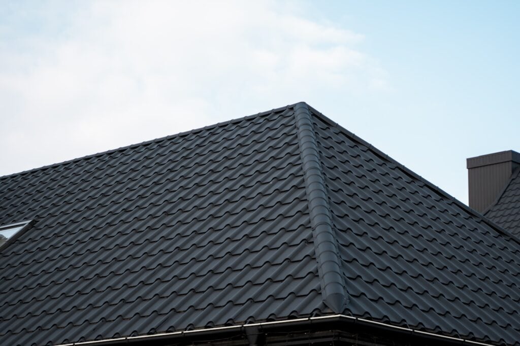 Black metal tile roof. Roof metal sheets. Modern types of roofing materials. Roof of the house, metal roof tile against the blue sky. Building