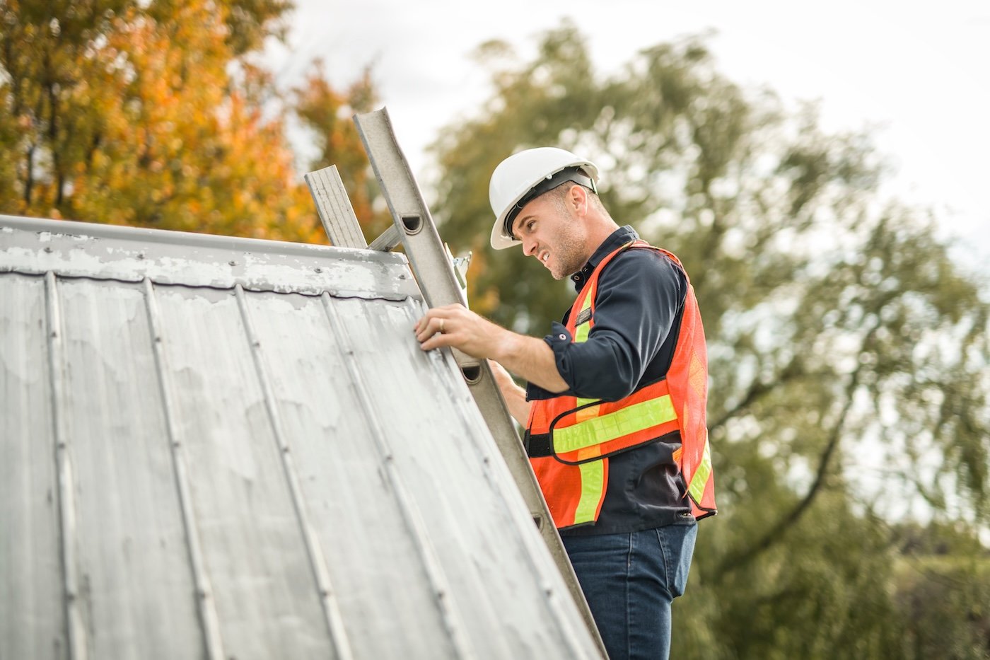 A man with hard hat standing on steps inspecting house roof