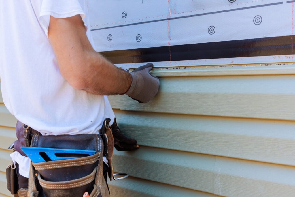 Worker installing vinyl PVC siding during construction on a facade new home