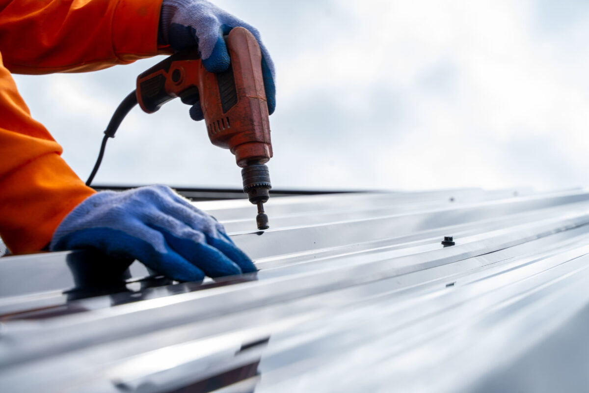 newark de commercial roofing Roofer worker using air or pneumatic nail gun and installing metal sheet on top of the new roof.