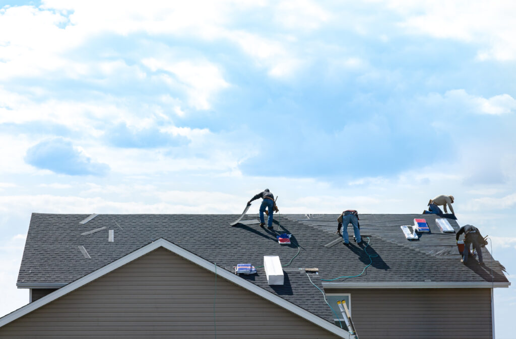 elkton residential roofing 4 construction workers fixing roof against clouds blue sky, install shingles at the top of the house. Renovate, improvement, build home exterior by professional teamwork. Safety and protection concept